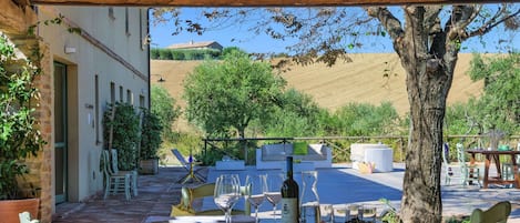 An outdoor dining area with a table set for two, surrounded by chairs, a potted plant, and a view of a hillside.