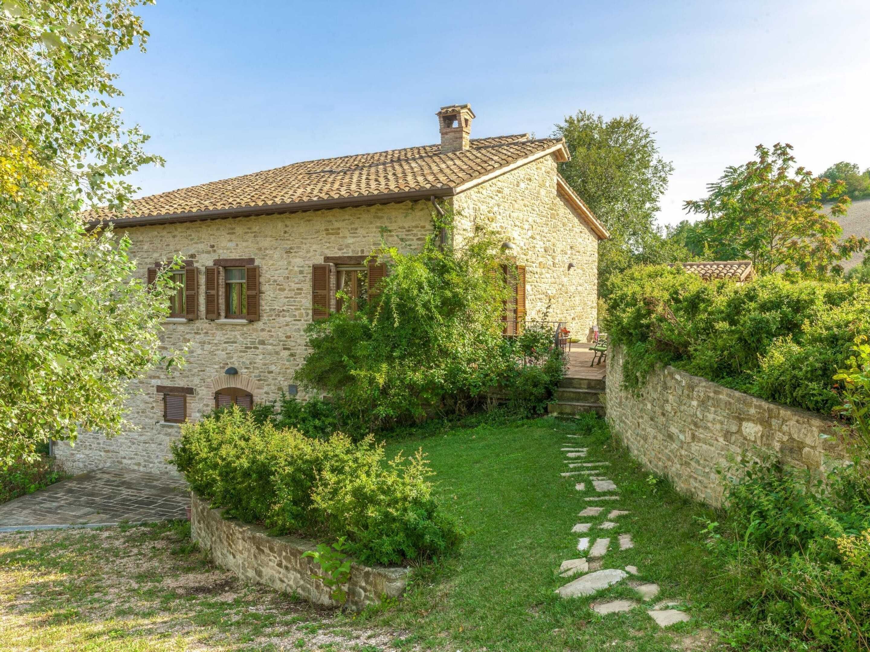 Una casa in pietra con tetto in tegole, circondata da un giardino e un muro in pietra.
