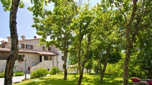 Un bâtiment en pierre, doté d’un toit en tuiles, entouré d’arbres et d’herbe verdoyants.
