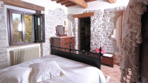 Une chambre à coucher avec un lit, une commode et un mur en pierre.