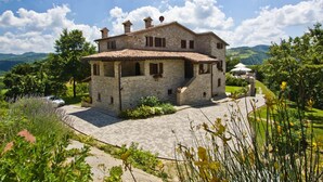 Une maison en pierre avec un toit en tuiles, entourée d’une allée pavée et d’une végétation luxuriante.