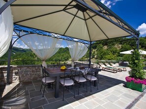 An outdoor patio with a covered dining area, stone flooring, and a view of the surrounding landscape. - Belvilla by OYO La Rocca (Apecchio)
