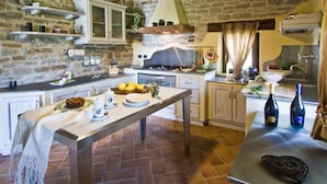 A rustic kitchen with stone walls, a wooden table set with plates and a bottle, and a hanging light fixture. - Belvilla by OYO La Rocca (Apecchio)