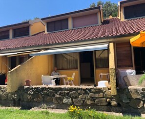 A two-story house with a stone wall foundation, a tiled roof, and a covered patio area with outdoor furniture. - Seaside Apartment With Views, Punta Ala (Castiglione della Pescaia)