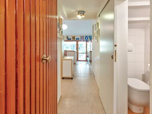 A hallway with a wooden door, a white toilet, and a kitchen area with a refrigerator and a cart. - Seaside Apartment With Views, Punta Ala (Castiglione della Pescaia)