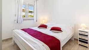Ein Schlafzimmer mit einem Bett, zwei Nachttischlampen, einem Fenster mit Vorhängen und einem Nachttisch mit Schubladen.