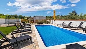 Ein rechteckiger Swimmingpool mit klarem, blauem Wasser, umgeben von Steinplatten und schwarzen Liegestühlen.