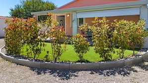 Ein modernes Gebäude mit rotem Dach und weißen Wänden, umgeben von einem gepflegten Garten mit verschiedenen Sträuchern und einer Rasenfläche.