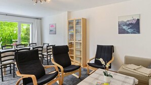 A room with a dining area, two black chairs, a sofa, a bookshelf, and a window with a view of greenery. - Ferienhaus Bergfreiheit (Winterberg)