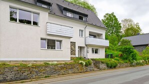 A two-story house with a stone facade, a balcony, and a well-maintained garden. - Ferienhaus Bergfreiheit (Winterberg)