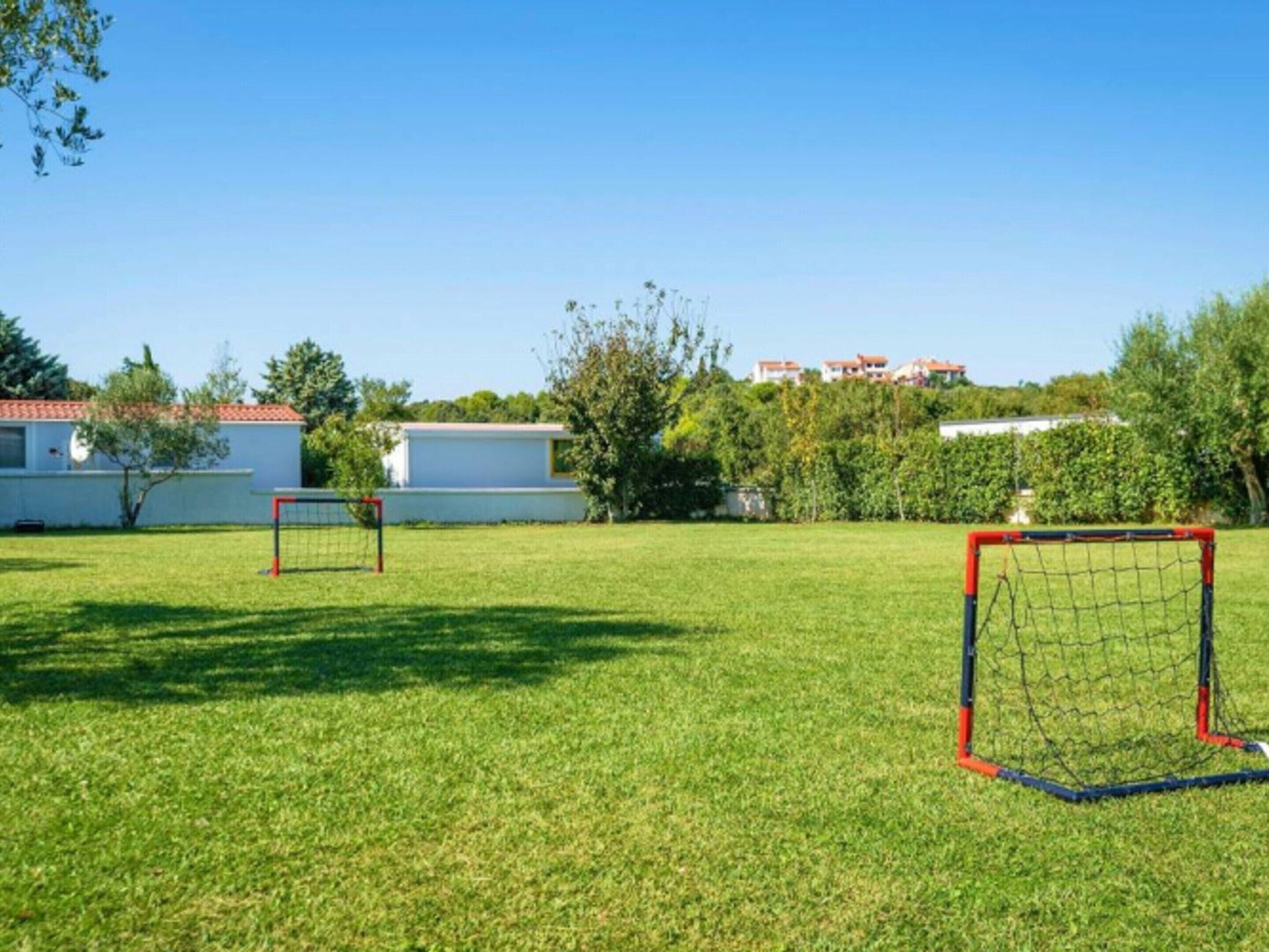 Ein grünes Feld mit zwei Fußballtoren und einem weißen Gebäude im Hintergrund.