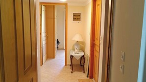 A hallway with wooden doors, a tiled floor, a small table with a lamp, and a framed picture on the wall. - Hillview Holiday Home in Kalavrouza (Nafpaktos)