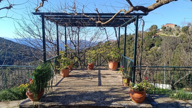 A stone-paved outdoor area with a metal pergola, potted plants, and a view of a mountainous landscape. - Hillview Holiday Home in Kalavrouza (Nafpaktos)