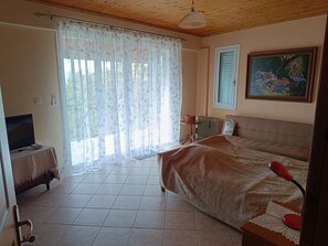Quarto com cama, televisão em uma mesinha de cabeceira, radiador e quadro na parede.
