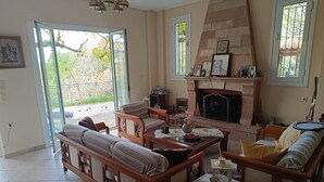 A spacious living room with a fireplace, comfortable seating, and a view through a glass door to a garden. - Hillview Holiday Home in Kalavrouza (Nafpaktos)