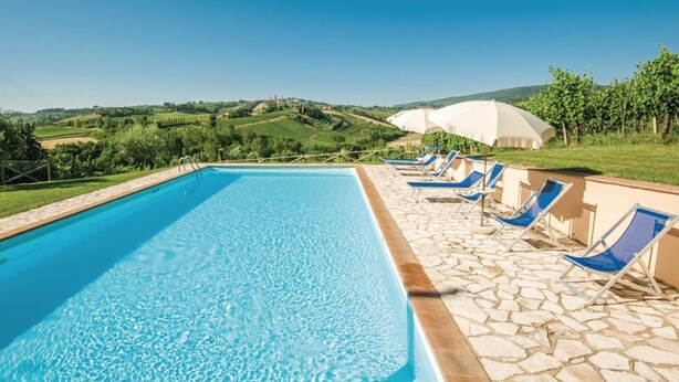 Una piscina con agua cristalina azul, rodeada de baldosas de piedra y sillas reclinables azules.