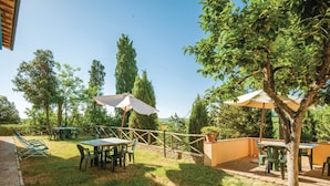 Un patio al aire libre con mesas y sillas, rodeado de árboles y una cerca de madera.