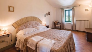 Un dormitorio con una cama grande, una silla, una ventana con cortinas y un radiador.