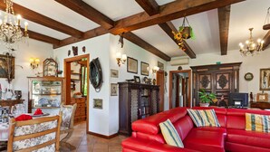 A spacious living room with a red leather sofa, wooden beams, and a chandelier. - Belvilla by OYO Villa Pratolina Agli Alberoni (Venice)