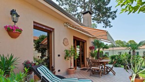 A patio with a wicker lounge chair, a wooden table, and potted plants. - Belvilla by OYO Villa Pratolina Agli Alberoni (Venice)