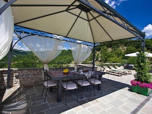 An outdoor patio with a covered dining area, stone flooring, and a view of the surrounding landscape. - Belvilla by OYO La Rocca Estate (Apecchio)