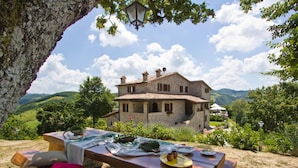 Ein Steinhäuschen mit Terrasse, umgeben von Grünflächen und Hügeln.