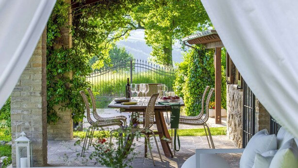 An outdoor patio with a table set for dining, surrounded by wicker chairs and a white sofa. - Marche Villa Close Culture (Fermignano)