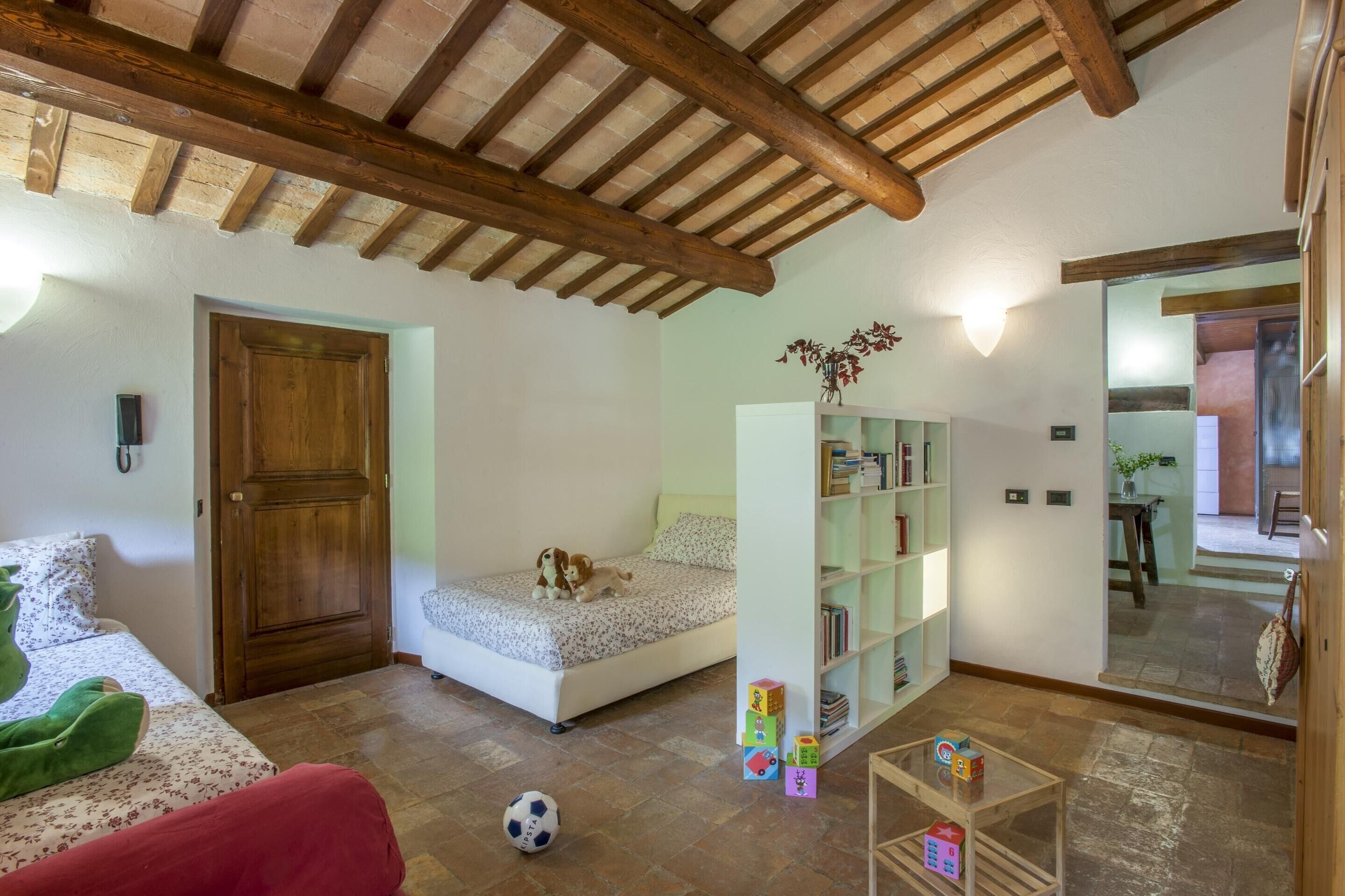 Ein Zimmer mit Holzbalkendecke, einem Bett mit Blumenmuster-Bettwäsche, einem Bücherregal und einem kleinen Tisch mit Spielzeug.