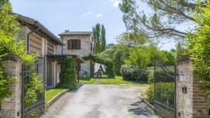 A gravel driveway leading to a stone house with a tiled roof, surrounded by lush greenery and a metal gate. - Marche Villa Close Culture (Fermignano)
