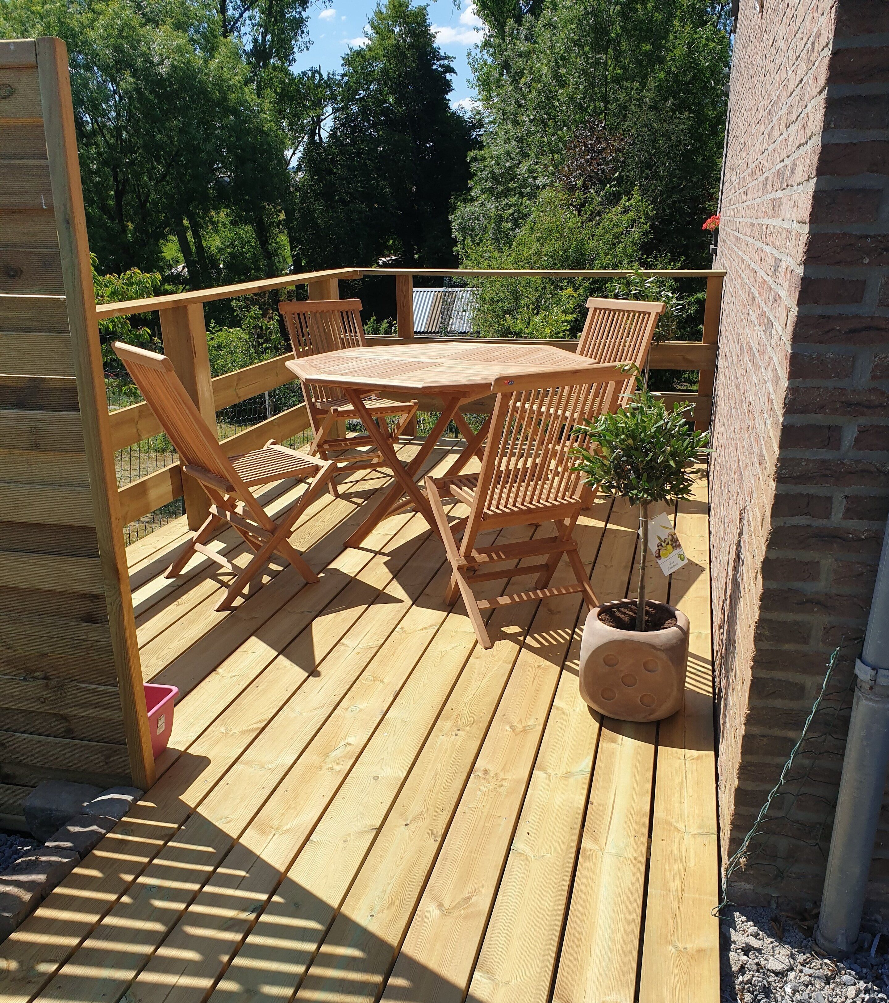 A wooden deck with a table and chairs, surrounded by a brick wall and greenery.