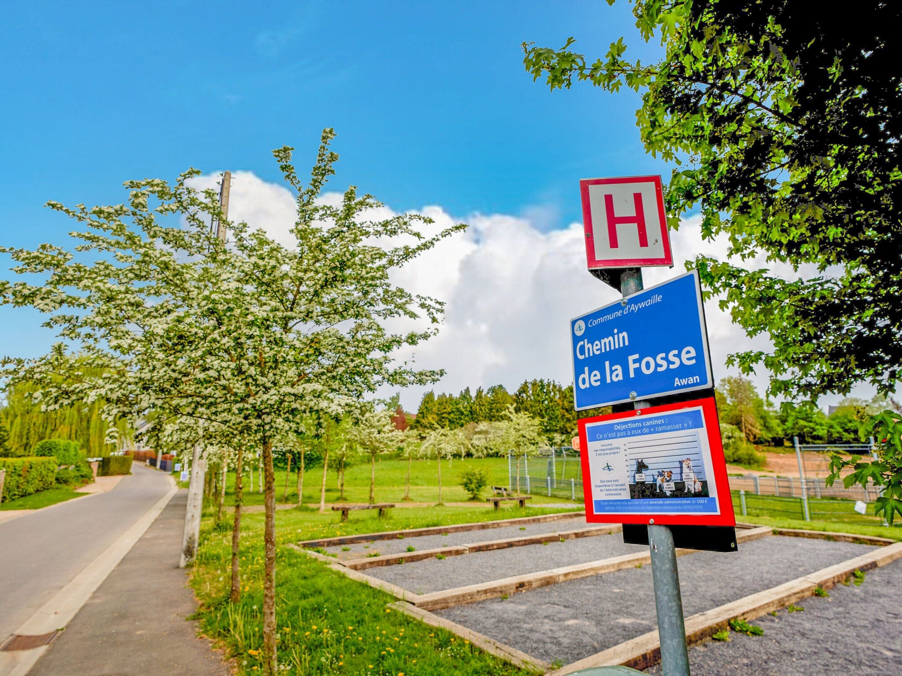 Wegwijzer met een rood H-symbool, een blauw bordje voor 'Chemin de la Fossé Awan', en een informatief bord in rood en wit.