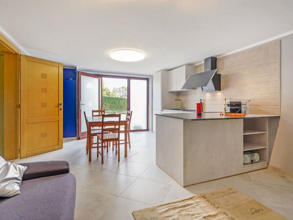 A modern kitchen with a dining area, a sofa, and a sliding glass door leading to a balcony. - Cottage in Aywaille With Garden (Aywaille)