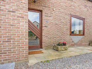 A brick building with a wooden door and a window. There is a stone planter with flowers next to the door. - Cottage in Aywaille With Garden (Aywaille)