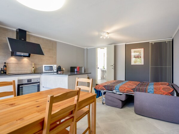 Cozy living space with a kitchenette, dining table, sofa, and small bed with storage bench.