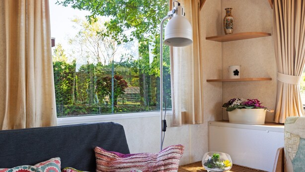 Une pièce chaleureuse avec un canapé, des coussins, une petite table sur laquelle est posé un vase, et une fenêtre avec des rideaux.