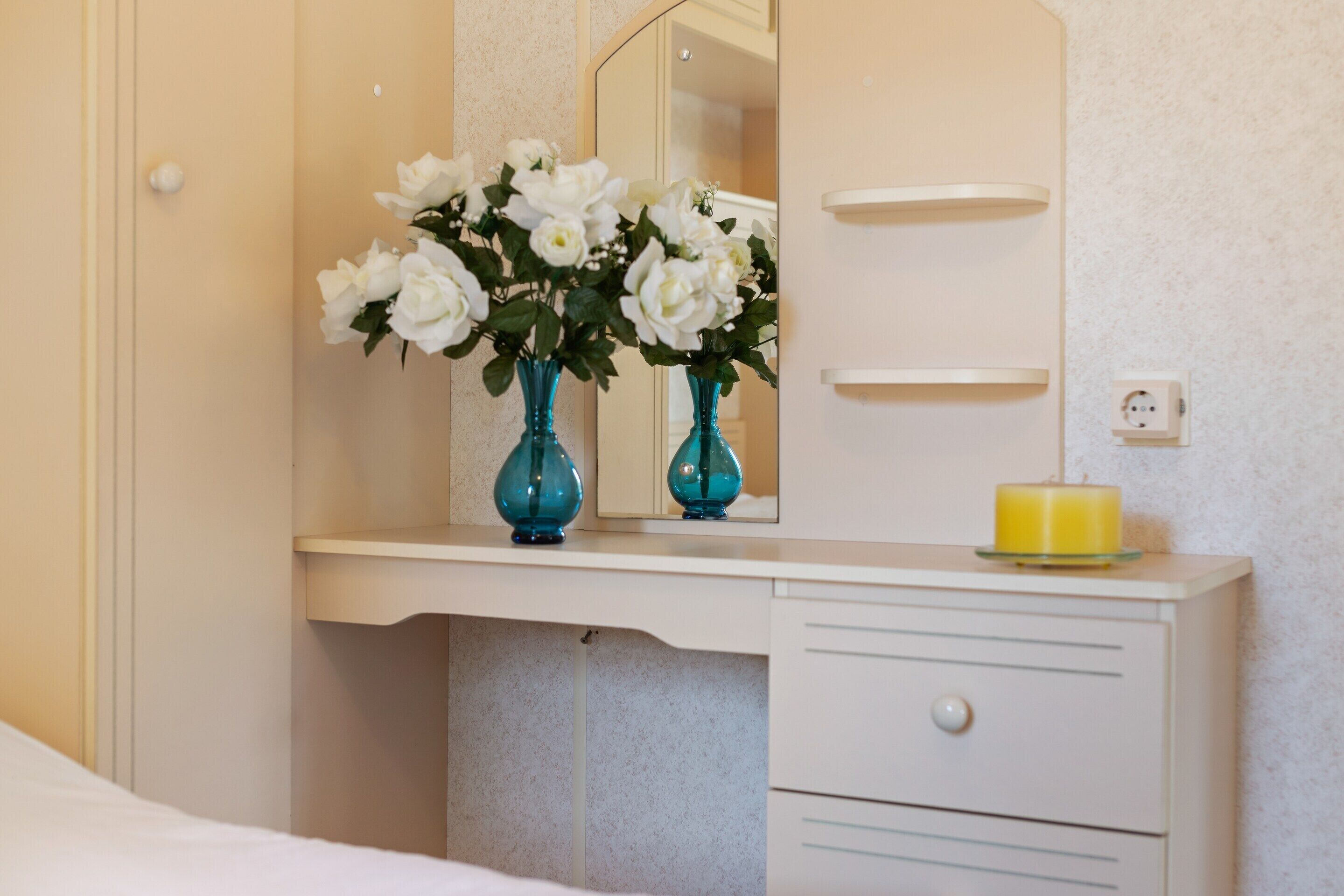 A bedroom with a white dresser, a mirror, and a vase with white flowers.