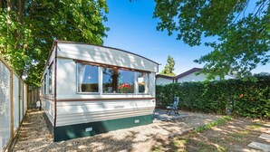 Une maison mobile avec une plaque signalétique, entourée d’un chemin de gravier et de verdure.