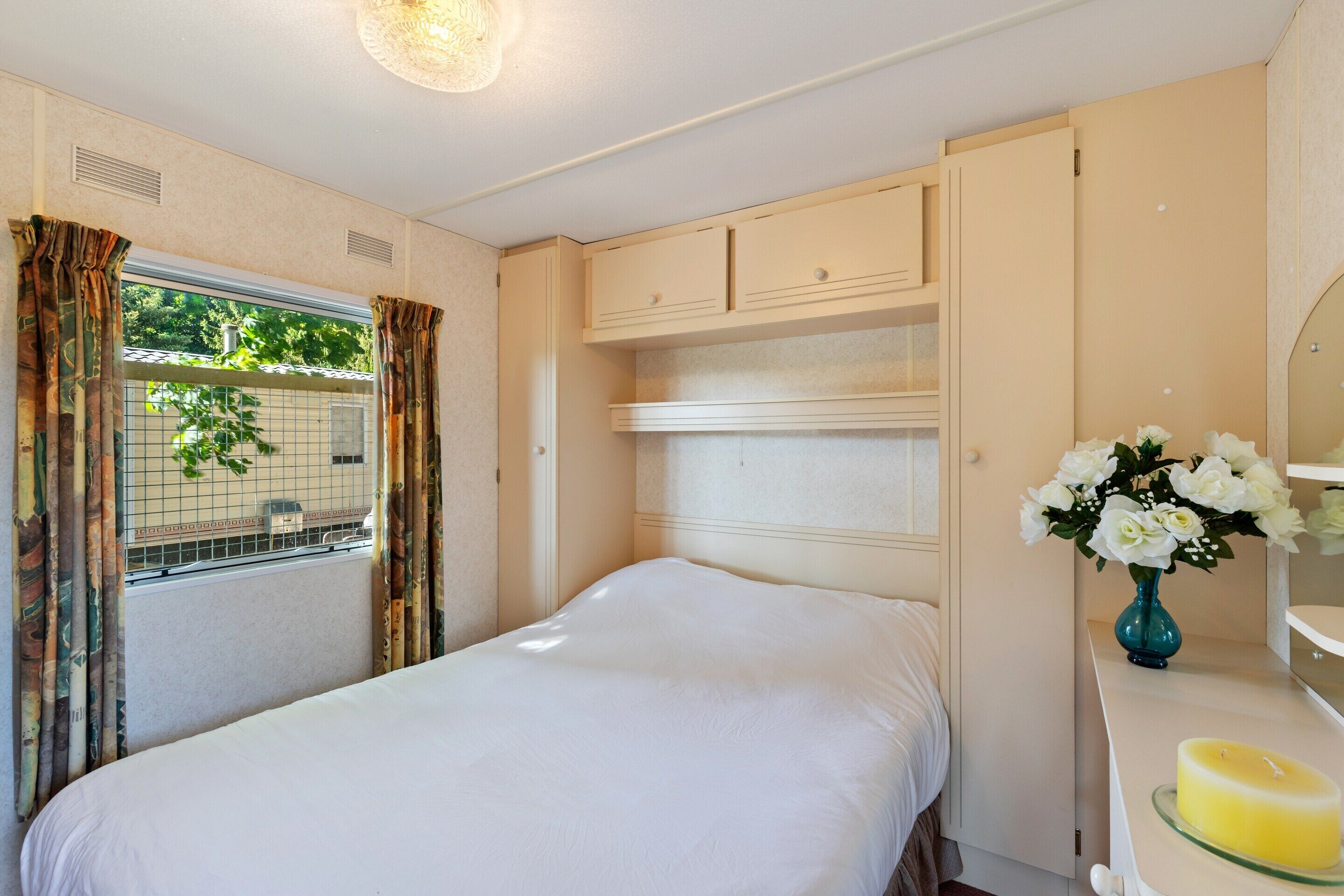 Un dormitorio con cama, cómoda, espejo y ventana con cortinas.