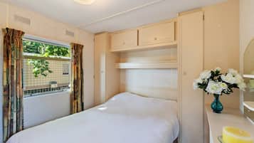 Un dormitorio con cama, cómoda, espejo y ventana con cortinas.