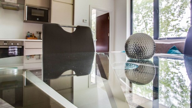 A modern kitchen with a glass dining table, stainless steel appliances, and a large window with a view of trees.