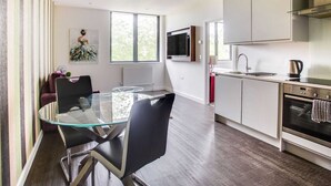 A modern kitchen with a glass dining table, stainless steel appliances, and a large window providing natural light.
