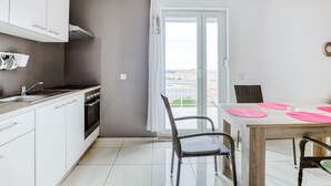 A modern kitchen with white cabinets, a stove, and a dining area with a table and chairs. - Comfortable Apartment in Novalja near Zrče Beach  (Novalja)