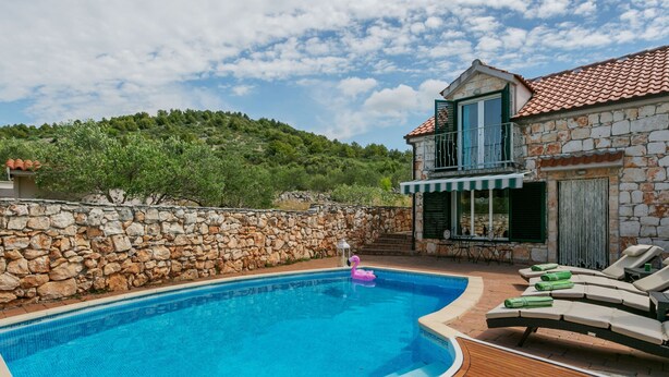 Piscina com deck de madeira, espreguiçadeiras e uma parede de pedra.