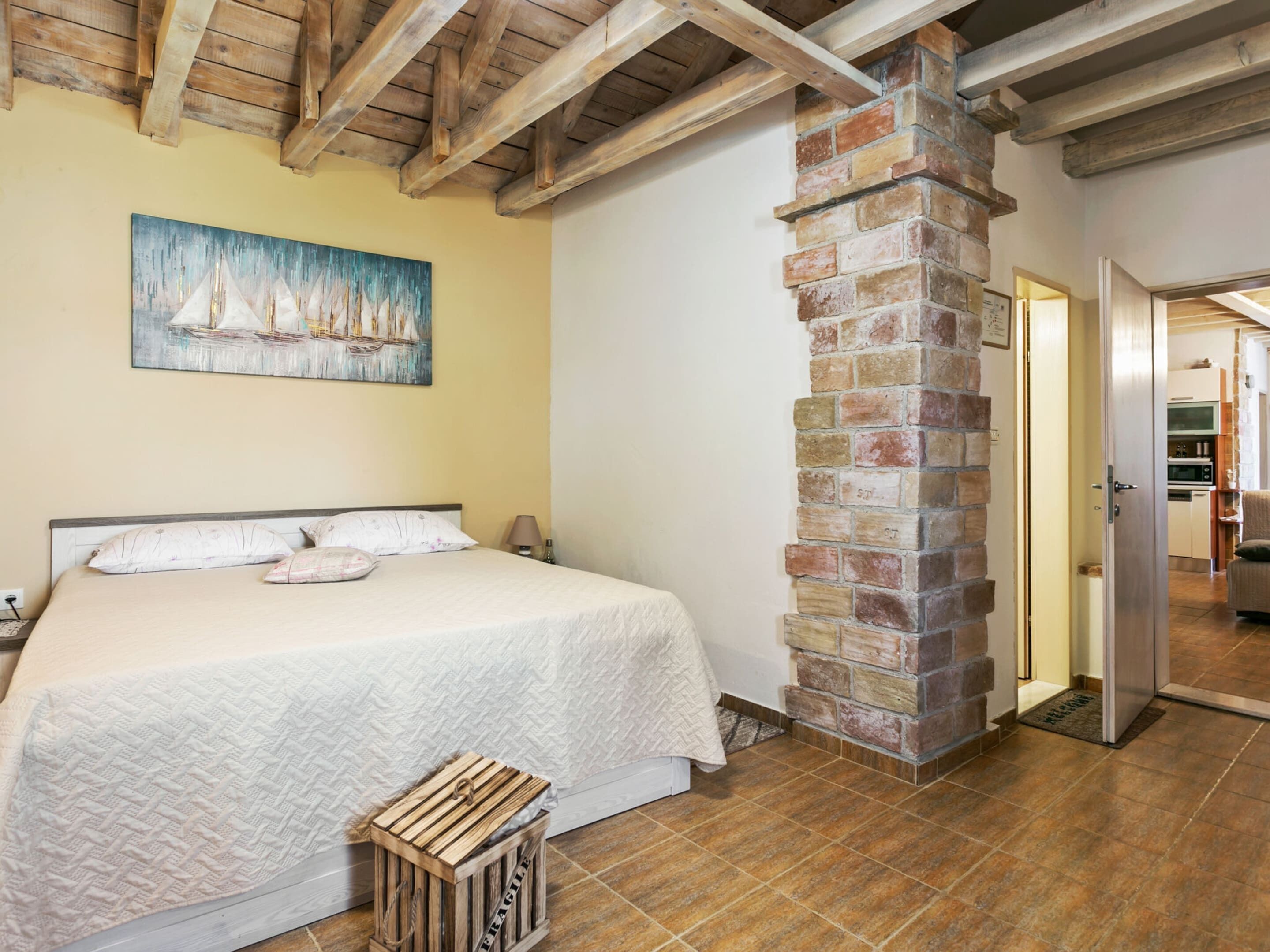 Un dormitorio con cama, un cofre de madera, chimenea de ladrillo y un cuadro en la pared.