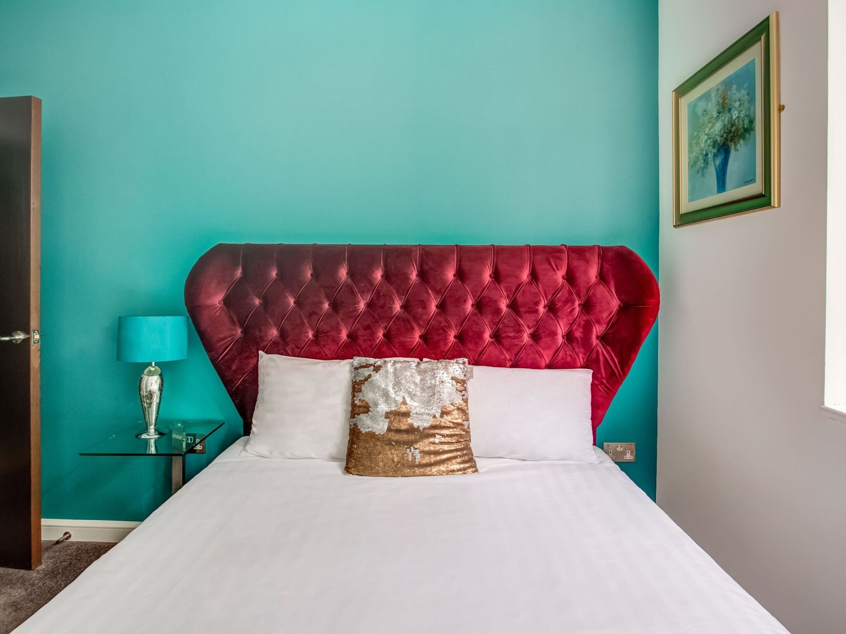 Een slaapkamer met een rood, gestapeld hoofdbord, witte beddengoed en een blauwgroene muur.