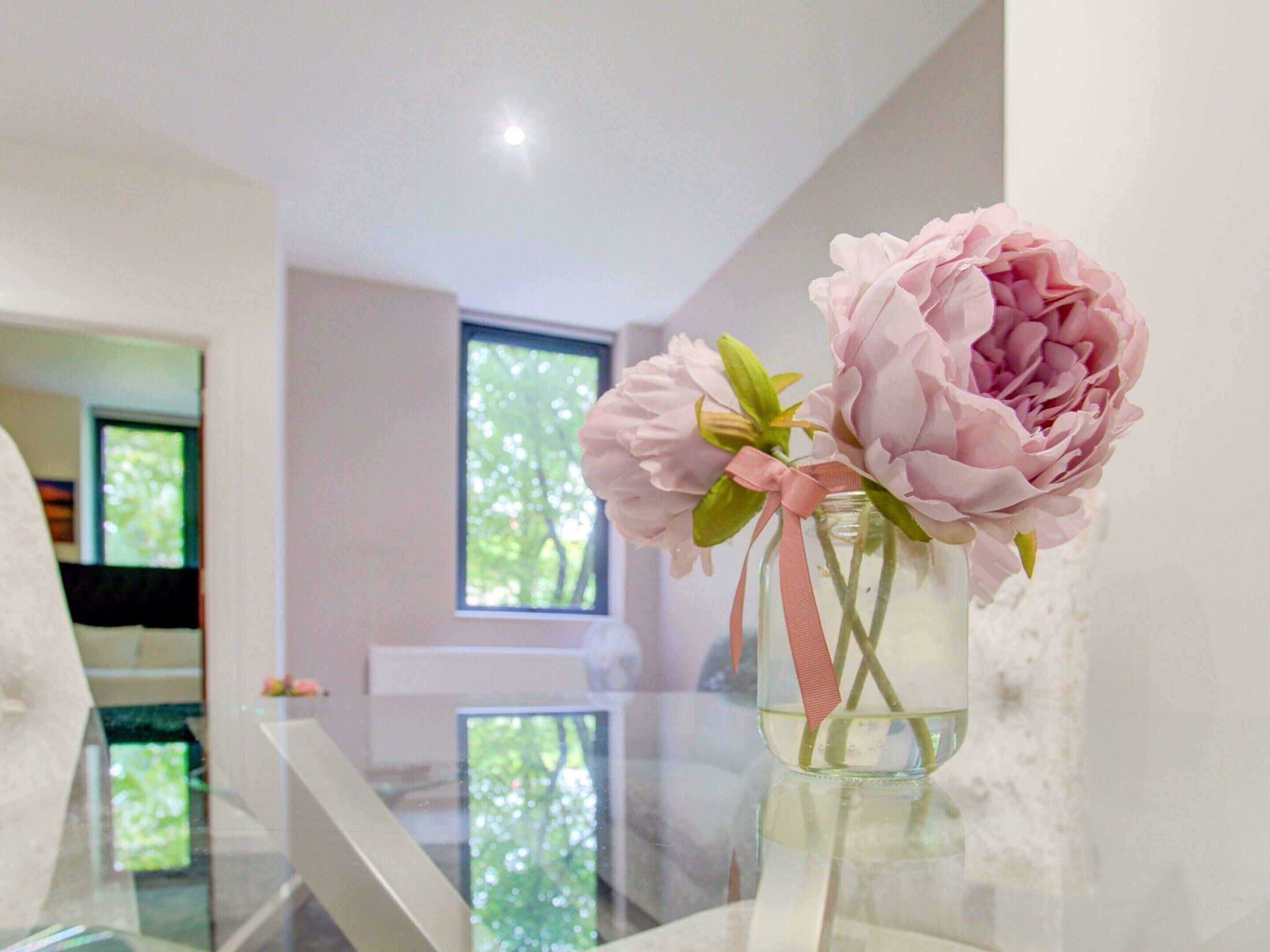 A clear glass vase with pink flowers on a reflective surface.