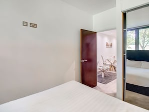 Une chambre d’hôtel moderne avec un lit simple, une porte en bois et une vue sur un espace repas comprenant une table et des chaises.