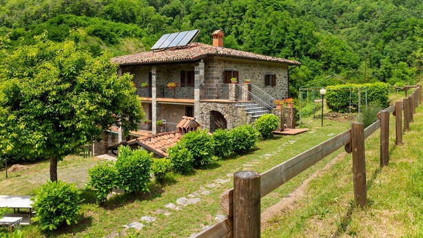 A stone house with a tiled roof, solar panels, and a wooden fence. - Belvilla by OYO La Casa sul Fiume First Floor (Fosciandora)