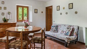 A dining area with a round wooden table, four chairs, a sofa with floral upholstery, and a window with a view of greenery. - Belvilla by OYO La Casa sul Fiume First Floor (Fosciandora)