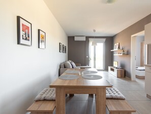 A modern living room with a wooden dining table, benches, and a sofa. There are framed pictures on the wall and a large window with curtains. - Apartment in Novalja Near Sea Beach (Novalja)